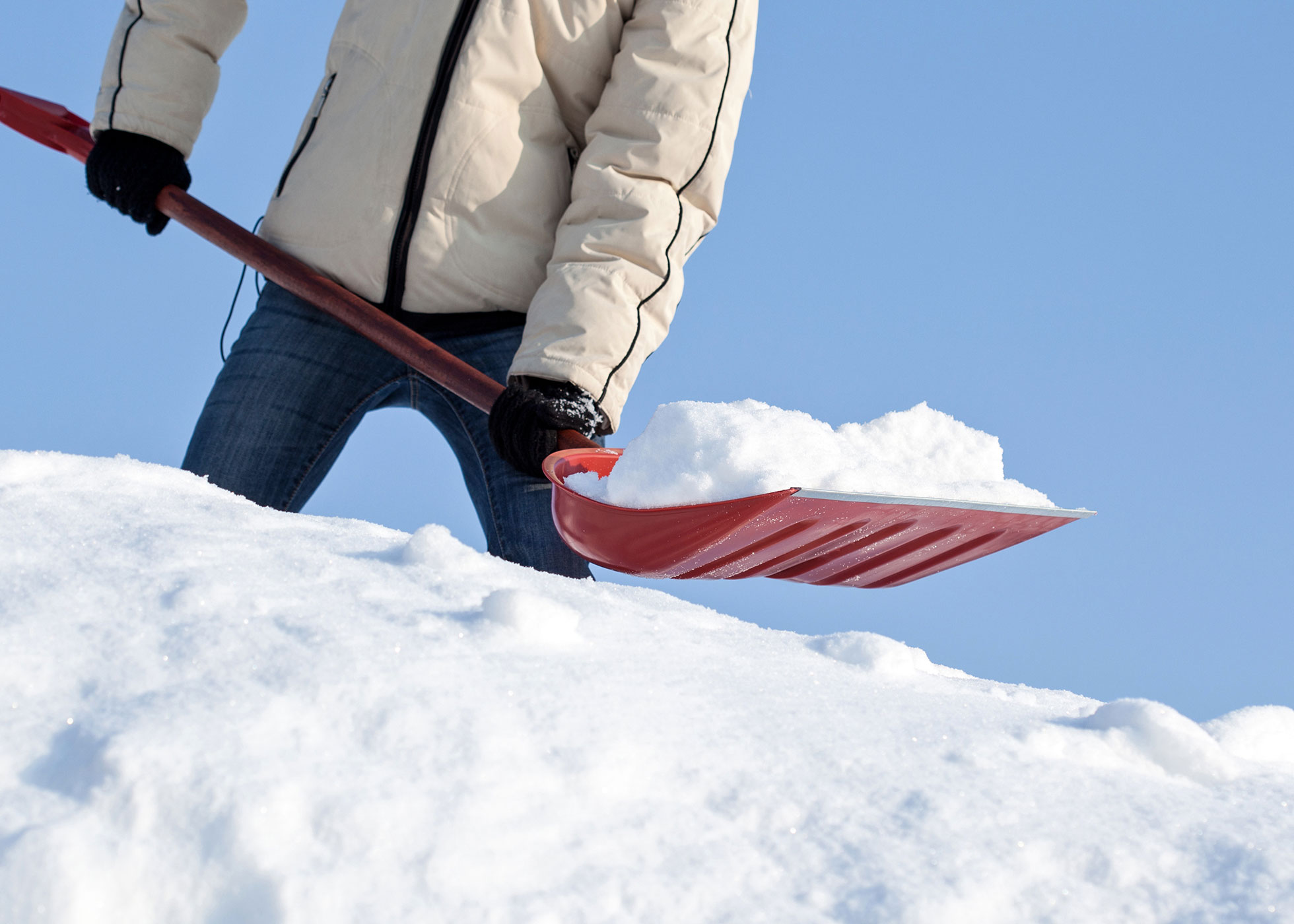 Une personne qui ramasse la neige avec une pelle rouge